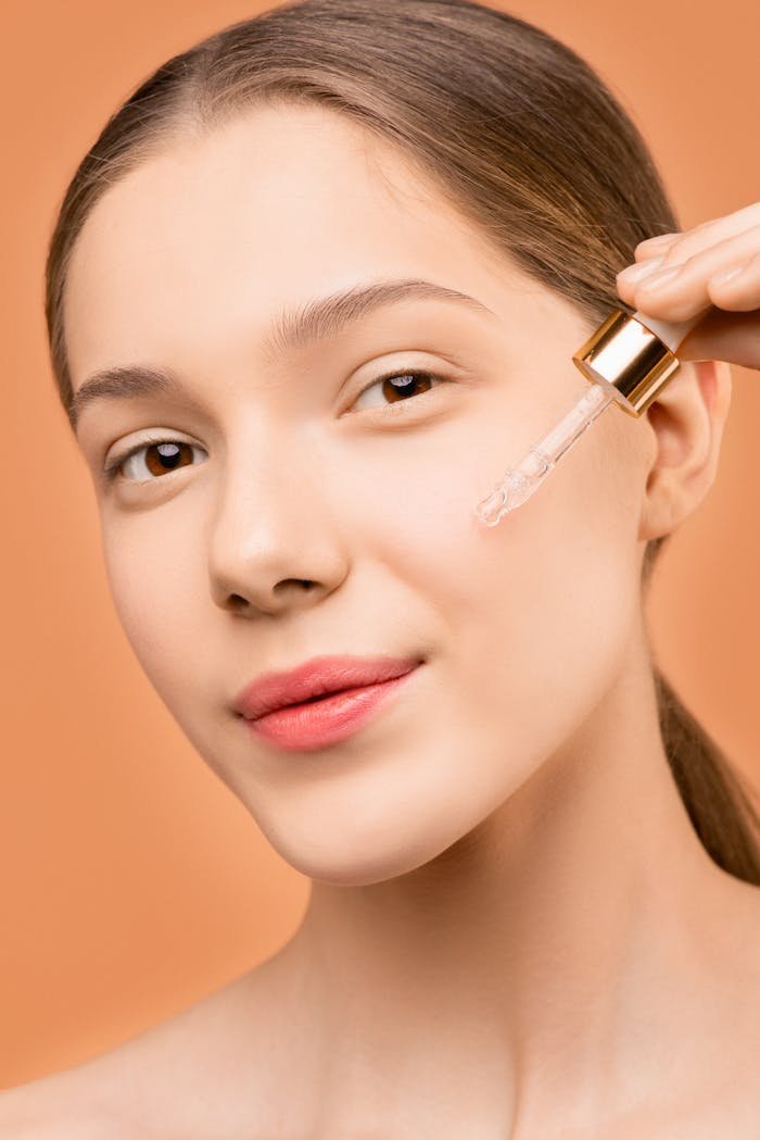 Close-up of a young woman using a dropper to apply facial serum for skincare treatment.